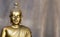 Golden antique buddha statue. The background is light slate gray. The face of the Buddha turned to the straight