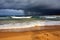 golden beach with view of crashing waves and stormy skies