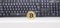 Golden Bitcoin coin standing on a white desk and in front of a black keyboard with highlighted keys. Plenty of negative