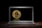 Golden bitcoin on the display of modern laptop in the dark room on wooden table. Cryptocurrency mining concept.