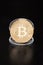 Golden bitcoin in transparent coin container on black