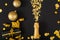 Golden bottle of champagne spills out gold sparkles in frame of gold festive Christmas decor confetti balls gifts on black