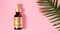 Golden bottle of hyaluronic acid resting on a pastel pink background next to a tropical green leaf