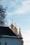 Golden brightly lit cupolas with orthodox crosses on top of a white stone church or cathedral are peeking from the dark stone old