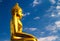 A golden Buddha statue sitting cross-legged on a slightly cloudy blue sky Add a filter to resemble an oil painting