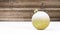 Golden christmas ball on wooden background with snowfall.