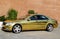 A golden-colored passenger car in the yard of the house near the garage on a clear sunny day. Automotive