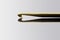 Golden crochet hook, old and well used, reflecting heart shape on shiny grey background.