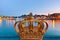 Golden crown on Skeppsholm bridge with illuminated Stockholm old city center Gamla Stan in the background during twilight sunset.