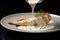 A golden-crusted salmon fillet garnished with dill, being drizzled with a creamy sauce on a white plate