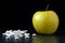 Golden delicious apple and different tablets and capsules on a black background with reflections. Health care, healthy eating and