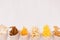 Golden different snacks on craft paper cone on soft white wood background, top view, border.