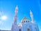 Golden-domed mosque with twin minarets against a clear blue sky. Sunlight Glistening on White Marble Mosque Minarets