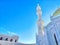 Golden-domed mosque with twin minarets against a clear blue sky. Sunlight Glistening on White Marble Mosque Minarets