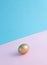 A golden egg isolated on a light pastel pink and blue background. Creative minimal Easter design.