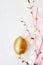 Golden egg on white background with pink branches, easter background with copy space