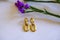 Golden elegant earrings on white wooden background across purple statice flowers. Top view. Copy space. Stylish flat lay