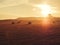 A golden field with haystacks on a mountain peak with a gazebo and tourists in the distance in a twilight haze and in