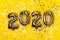 Golden foil balloons on yellow background with sparkles. Inflatable numbers 2020. Holiday Christmas concept