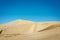 Golden hills of Giant sand dunes under cloudless blue sky. Tiny figures of people climbing up the dunes demonstrate the