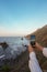 Golden Hour Serenity: Close-Up of Hands Holding a Smartphone, Framing a Scenic Coastal Landscape with Rocky Cliffs and Ocean Waves