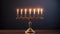 Golden menorah with seven gold candles lighting on dark background.