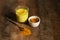 Golden Milk in a glass cup. Next to it is turmeric for making a drink and a spoon with spices. Dark background