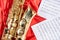 Golden musical instrument alto saxophone on red fabric with music sheets