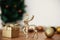 Golden reindeer, gift box and glitter bauble toys on background of christmas tree with lights on rustic background. Merry