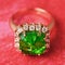 The Golden Ring with a big emerald and a path from small cubic zirconias on a red abstract background