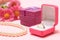 Golden ring in box, gift box, beads and flowers on a pink background.