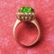 Golden ring with large emerald and small cubic zirconias on a red abstract background