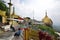 Golden rock on right & temple building on left with little buddhist monks coming from the right at Kyaiktiyo Pagoda