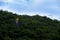 Golden sacred rock at Wat Thewarup Song Tham, Thailand surrounded by forest under the blue sky.