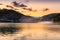 Golden sky and dramatic fluffy clouds over reflective, silky lake and dust cloud flying over the water