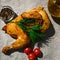 Golden smoked chicken in oil on white food paper is decorated with tomatoes, a sprig of greens, pepper and oil.