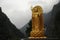 Golden standing Buddha statue surrounded by mountains