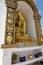 A golden statue of Buddha sitting in the lotus position, located in a niche surrounded by traditional Buddhist designs