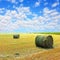 Golden stubble field and hay bales against cloudy sky.