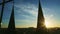 Golden sun hiding behind dark silhouettes of high church spires against blue sky