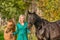 In the golden sun a portrait of a blond smiling girl with her horse and foal in the forest. Wearing a green dress. Selective focus