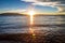 Golden sun stars reflect off the surface of glassy water while the sun is setting behind flat mountains in the distance