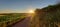 Golden sunrise shining overt the hills, corn plantations and the narrow road