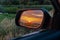 A golden sunset seen in an outside rear view mirror