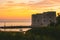 Golden sunset in the town of Dubrovnik, castle standing on the shore of a small harbour, sailboat leaving the harbour and a small