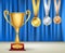 Golden trophy cup and set of medals with ribbons on blue curtain