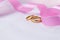 Golden wedding rings for engagement. Marriage golden rings with white, pink ribbons background. Rings on the white and red rose.