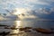 Golden Yellow Sun with Bright Sunlight rising from behind Clouds with Reflection in Sea Water - Morning Sky at Beach