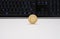 Golen Bitcoin coin standing on a white desk and in front of a black keyboard with highlighted keys