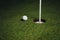 Golf ball nearby hole with pin flag, green grass background